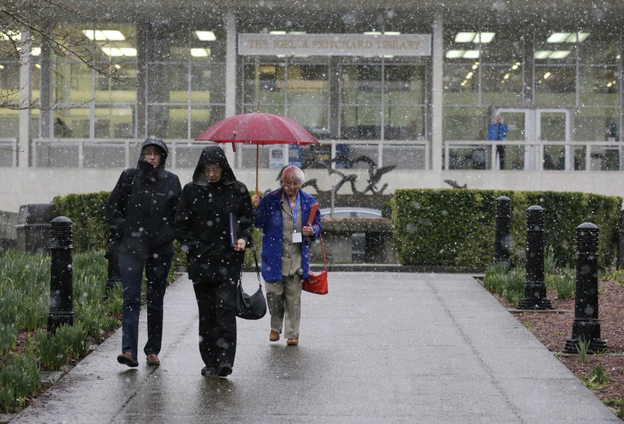Pedestrians walk in front of the Washington State Library during a brief snow shower Feb. 23 at the Capitol in Olympia. (AP Photo/Ted S.