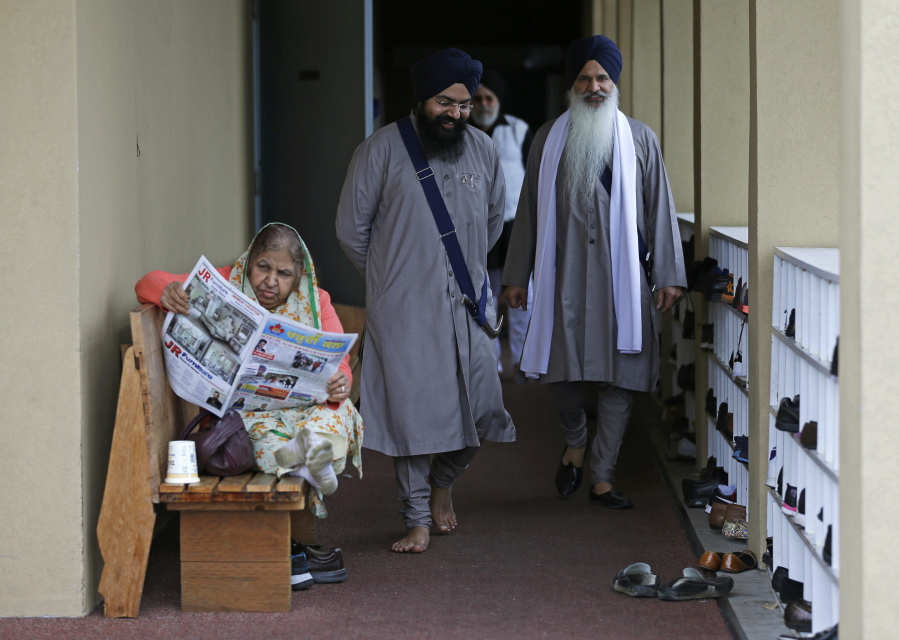 Men walk past a woman reading a newspaper at the Gurudwara Singh Sabha of Washington, a Sikh temple in Renton. (Ted S.