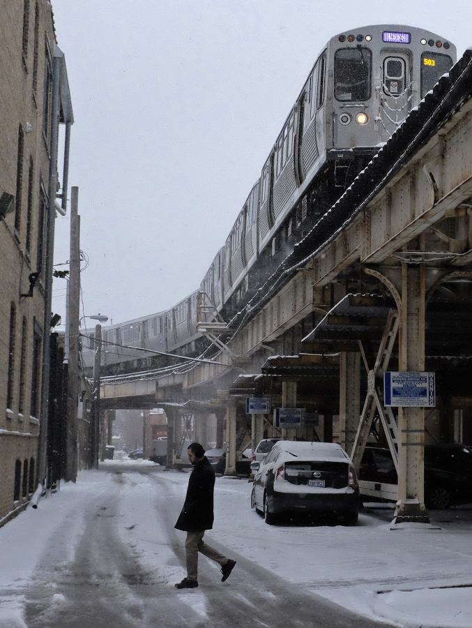 A commuter walks through the snow-covered sidewalk as the train passes along Monday in Chicago. The Chicago area and much of Illinois are getting snow as part of a storm hitting the Midwest and beyond.
