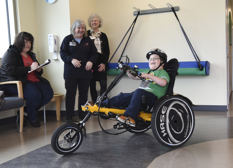 Holdyn Hanset, 7, rides an adaptive bike around the indoor track at Legacy Children&#039;s Center while his mom, Holly Hanset, from left, pediatric rehabilitation manager Lisa Lyons and Shirley Gross with the Salmon Creek Hospital Foundation watch. The rehab program didn&#039;t have the space for adaptive bikes before completing its 3,425-square-foot expansion.