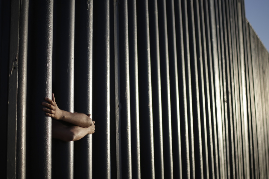 The hands from Daniel Zambrano of Tijuana, Mexico, hold on to the bars that make up the border wall separating the U.S. and Mexico as the border meets the Pacific Ocean in San Diego.