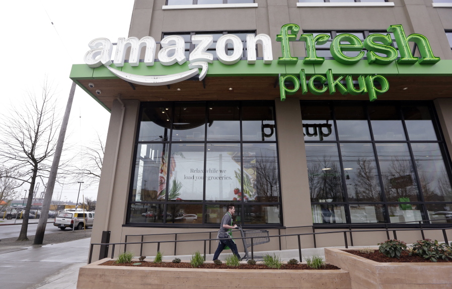 An Amazon worker wheels back a cart March 28 after loading a bag of groceries into a customer&#039;s car at an AmazonFresh Pickup location in Seattle.
