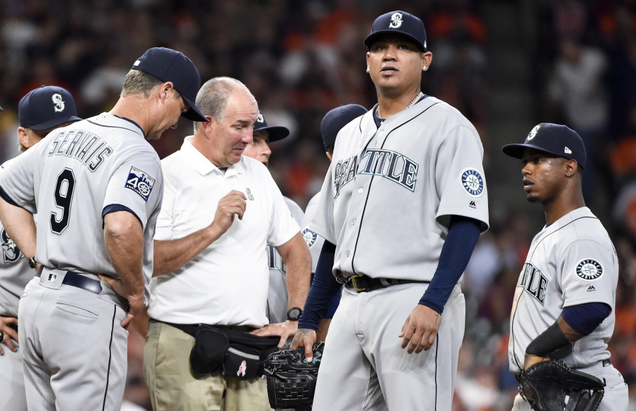 Seattle Mariners starting pitcher Felix Hernandez, second from right, is checked out by manager Scott Servais (9) and a trainer in the fourth inning of a baseball game against the Houston Astros, Monday, April 3, 2017, in Houston.