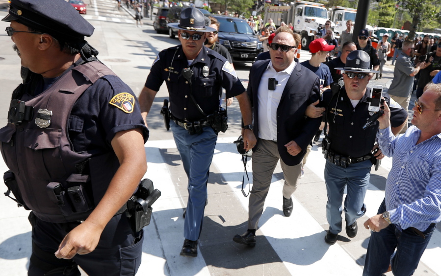 Alex Jones, center right, is escorted by police out of a crowd of protesters outside the Republican convention in Cleveland in July.