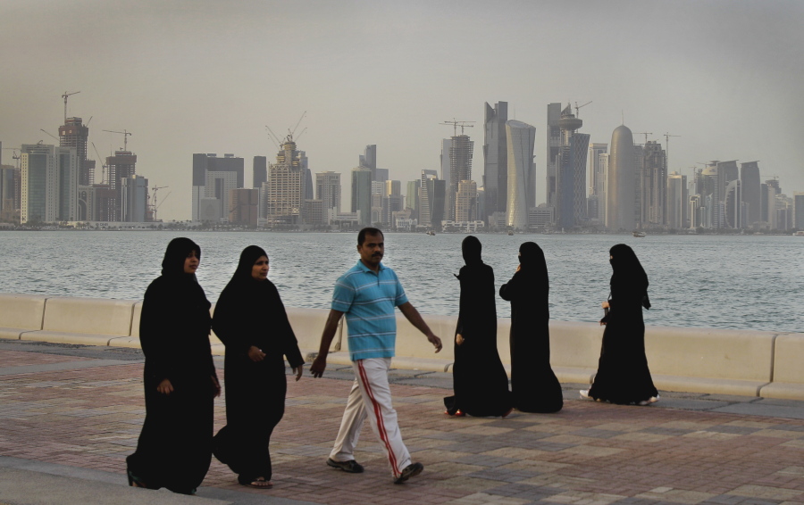Eith the new high-rise buildings of downtown Doha in the background, Qatari women and a man enjoy walking by the sea, in Doha, Qatar.