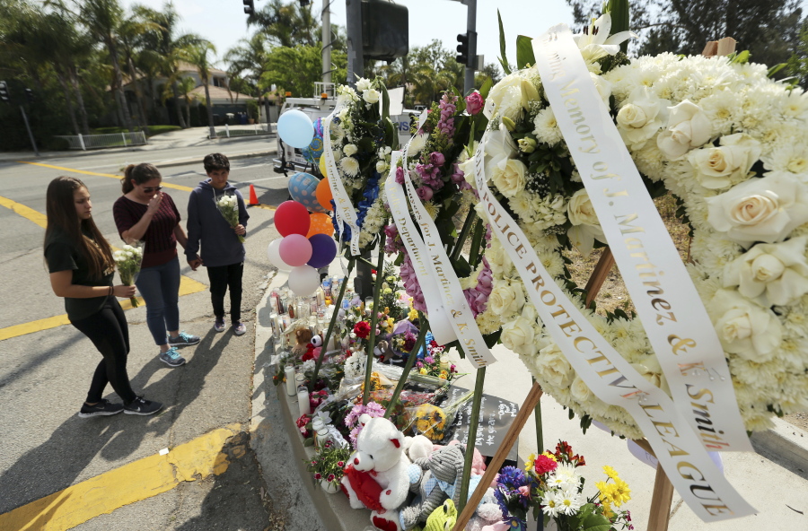 People pray before placing flowers at a sidewalk memorial to the teacher and student who were shot to death Monday at North Park Elementary School in San Bernardino, Calif., Tuesday, April 11, 2017.