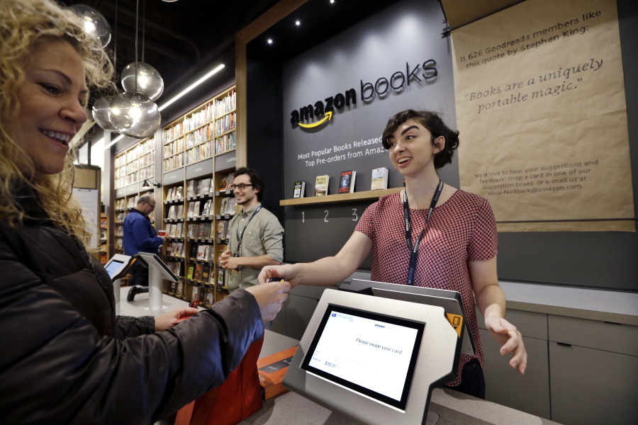 Customer Kirsty Carey, left, gets ready to swipe her credit card for clerk Marissa Pacchiarotti, as she makes one of the first purchases at the opening day Nov. 3, 2015 for Amazon Books, the first brick-and-mortar retail store for online retail giant Amazon, in Seattle.
