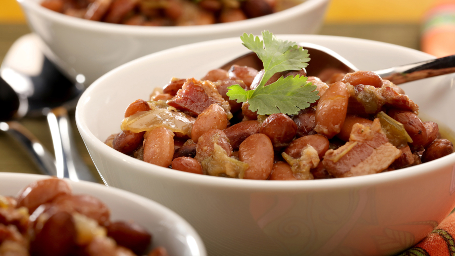 Pinto beans are cooked with bacon, then served with grated cheese and fresh cilantro.