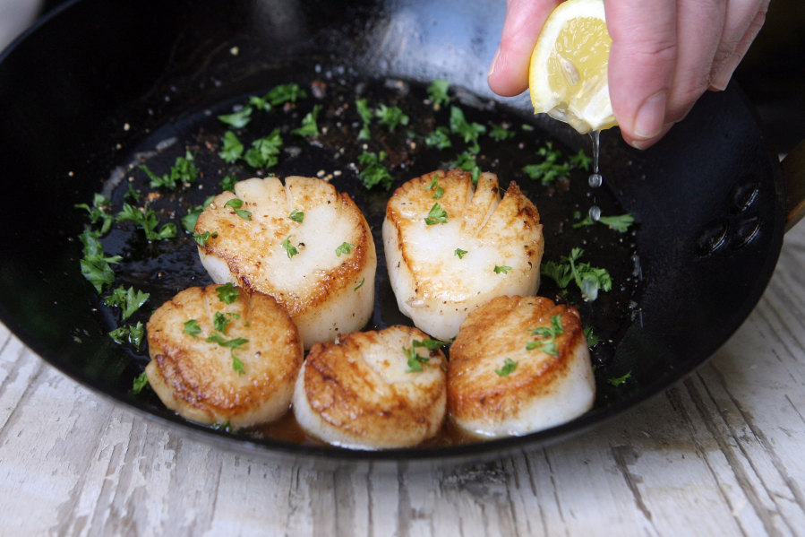 Squeeze a bit of lemon on seared scallops in the pan with butter and parsley garnish. (Hillary Levin/St.