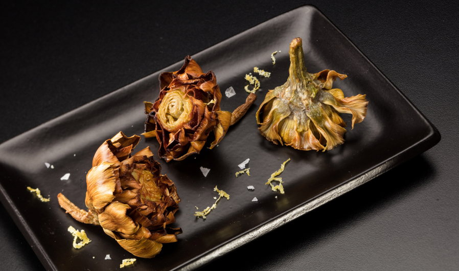 Baby artichokes are poached in oil, then crisped up in oil again before serving, sprinkled with a lemon zest and salt seasoning.