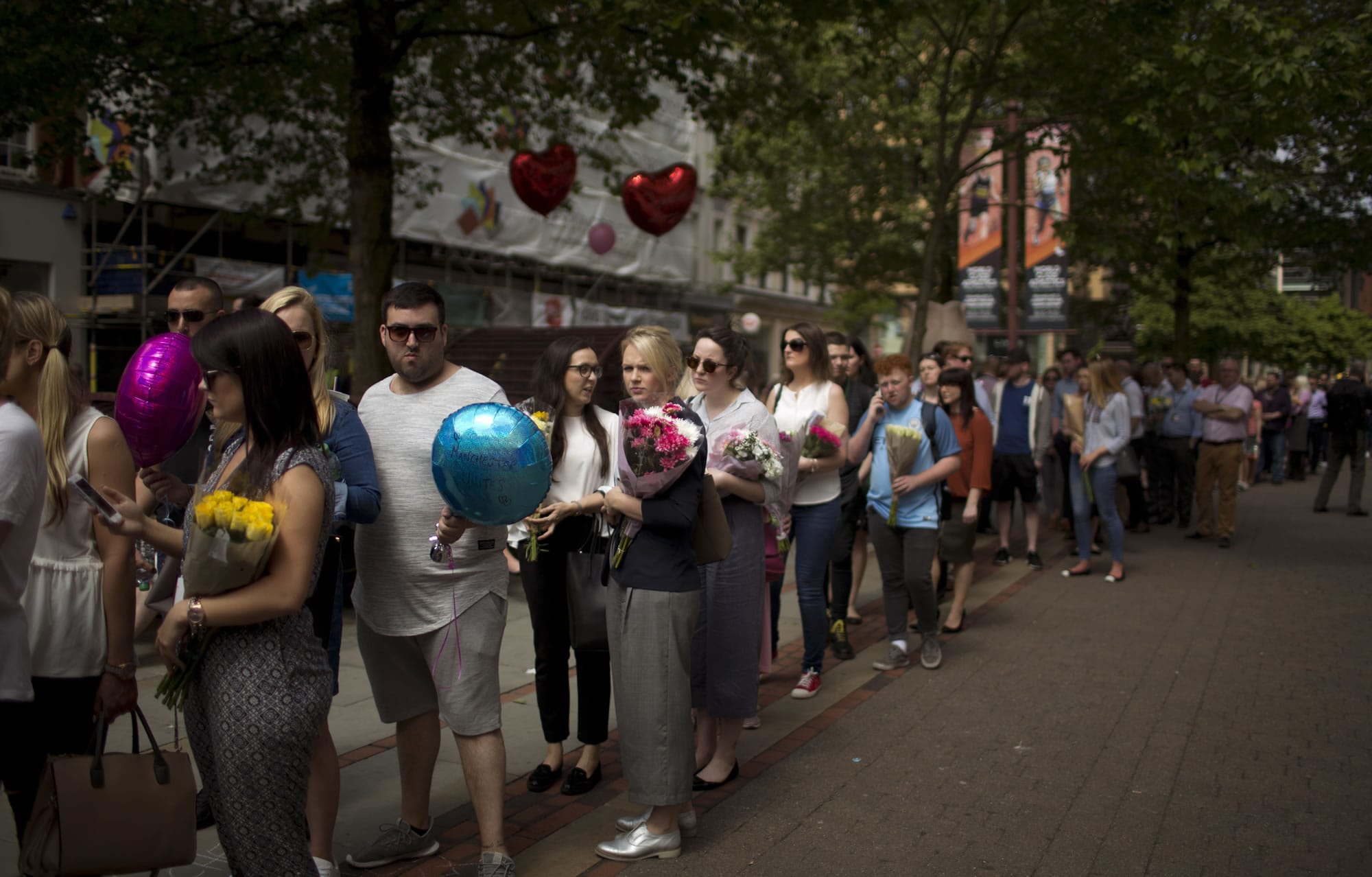 People queue to place flowers at St Ann's square in central Manchester, England Thursday May 25 2017. More than 20 people were killed in an explosion following a Ariana Grande concert at the venue late Monday evening. Britons will find armed troops at vital locations Wednesday after the official threat level was raised to its highest point.