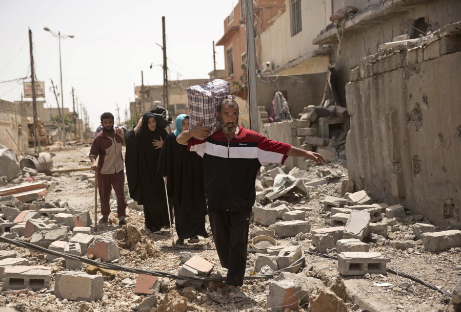 Iraqi civilians walk through rubble May 15, 2017, as they flee fighting between Iraqi special forces and Islamic State militants, in western Mosul, Iraq. The United States is looking ahead toward a decisive battleground in its bid to destroy the Islamic State group, even as U.S.-backed local forces must still finish the fight for the extremists’ two main strongholds in Iraq and Syria.