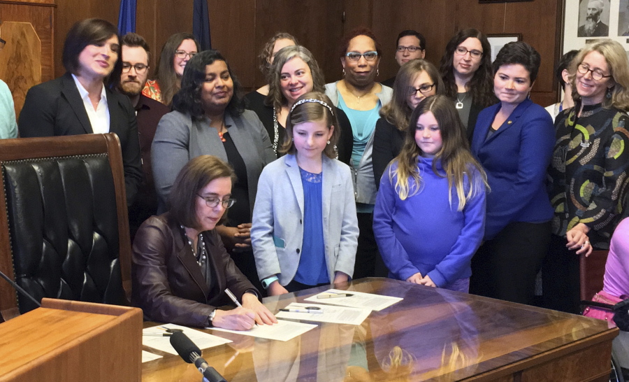 Gov. Kate Brown, seated, signs House Bill 2673 in Salem, Ore., Wednesday, May 31, 2017, making the process more private for transgender individuals to change their birth certificate records. The new law makes Oregon the second state with an alternative option for transgender people to update their birth records.
