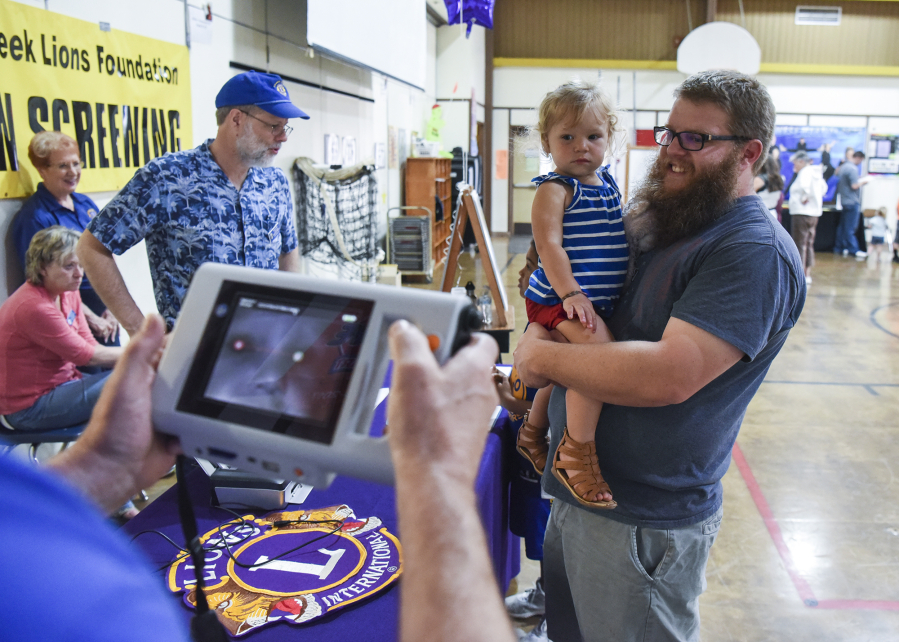 Andy Pyle, right, holds his daughter, Georgia, 2, as her vision is tested by a Salmon Creek Lions Club member Friday at Truman Elementary School in Vancouver.