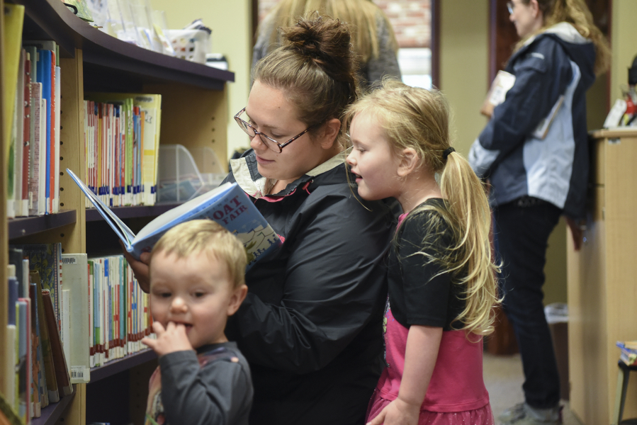 Jahara Craber, center, looks at a book with her daughter, Alleyah Sansburn, 4, while her 18-month-old son Liam Sansburn listens nearby May 30 at the Yacolt Library Express.