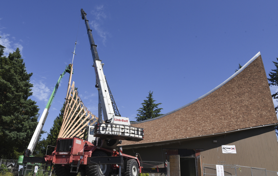 A crane holds a cross over the roof of First Congregational United Church of Christ in Hazel Dell while workers in a construction basket secure it into place.