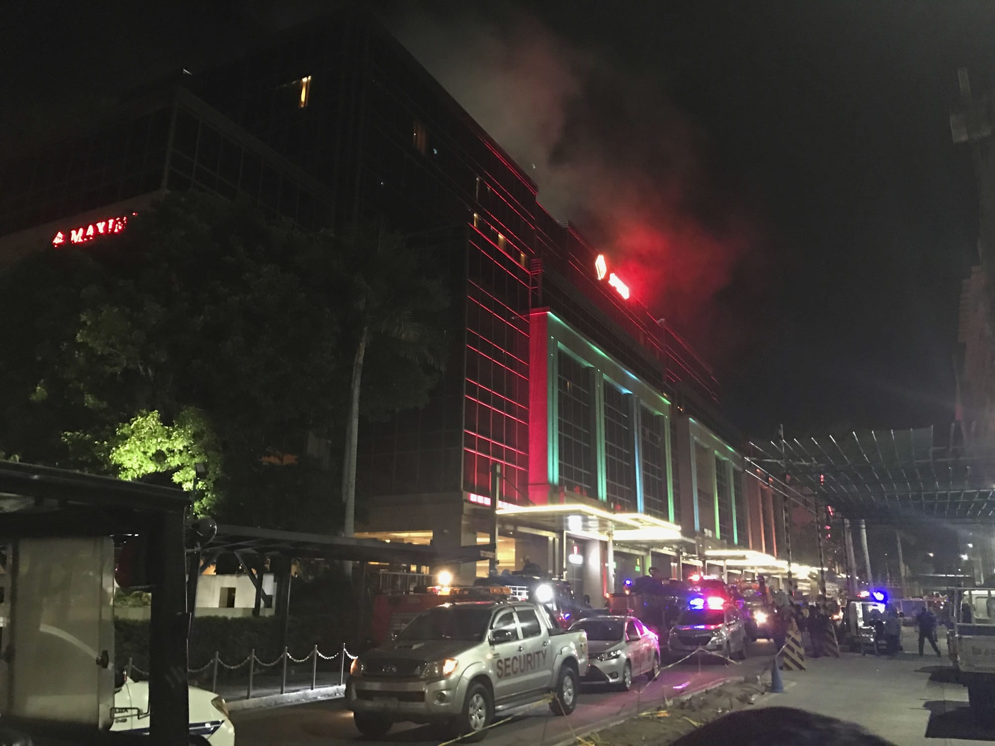 Emergency responders and security officials are parked outside as smoke rises from the Resorts World Manila complex, early Friday, June 2, 2017, in Manila, Philippines. Gunshots and explosions rang out early Friday at a mall, casino and hotel complex near Manila's international airport in the Philippine capital, sparking a security alarm amid an ongoing Muslim militant siege in the country's south.