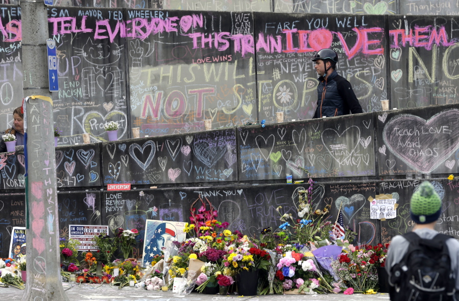 A bicyclist walking his bike down a ramp in Portland on Wednesday is surrounded by messages, flowers, images and candles at the memorial for two men fatally stabbed on a MAX train last week.