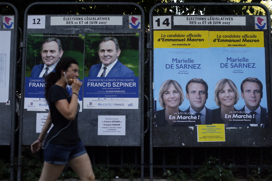 A woman walks past electoral posters displaying posters of the parliamentary elections Sunday in Paris, France.