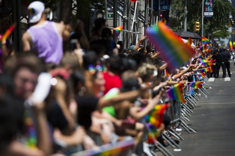 Member of the crowd line the street with rainbow flags as they watch the New York City Pride Parade on Sunday.