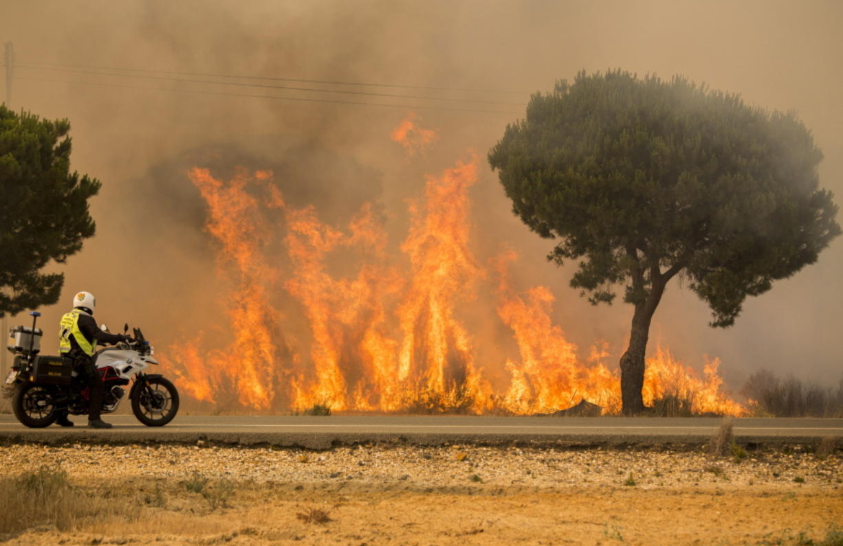 A military police officer stands by his motorcycle next to flames from a forest fire near Mazagon in southern Spain, Sunday June 25, 2017. A forest fire in southern Spain has forced the evacuation of around 1,000 people and is threatening Donana National Park, one of Spain's most important nature reserves and a UNESCO World Heritage site since 1994, and famous for its biodiversity, authorities said Sunday.