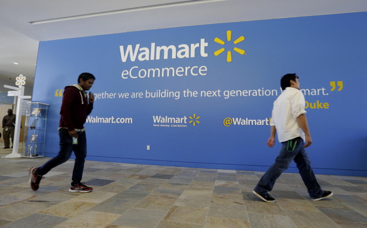 Two Wal-Mart employees walk past a sign in the lobby at the Walmart.com office in San Bruno, Calif.