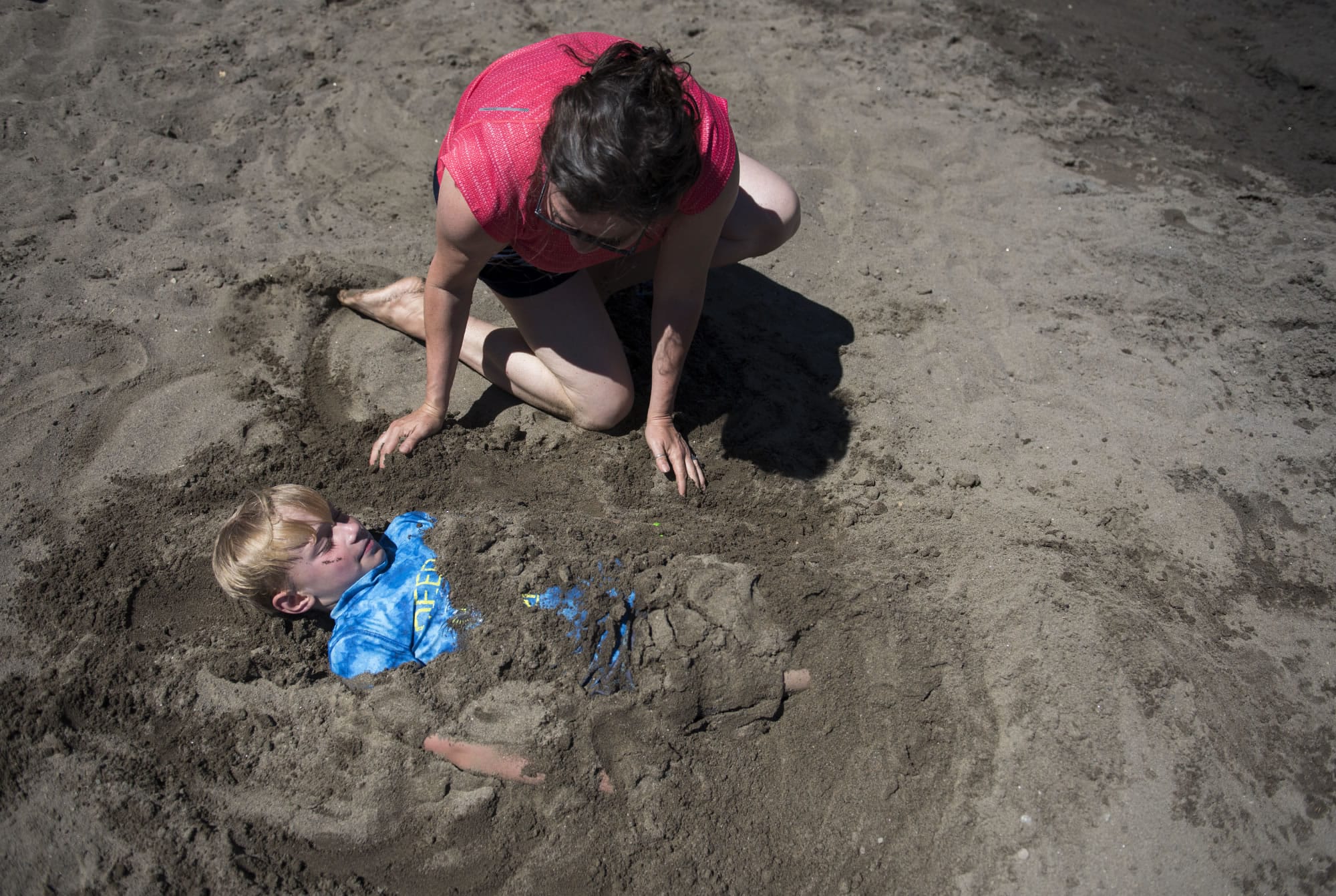 Heather Hale of Japan spreads sand over her nephew Andrew Hisel of Vancouver, 7, at Klineline Pond in Salmon Creek on Monday afternoon. A heat wave is moving through the area this week with triple-digits forecast for Wednesday and Thursday.
