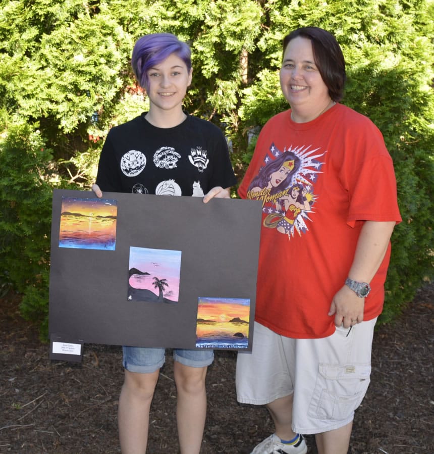 Washougal: Jemtegaard Middle School seventh-grader Adel Cathey, left, and Dani Allen, Jemtegaard art teacher, with Adel’s three watercolor sunset paintings, which district staffers honored her for by hanging them in the district office.