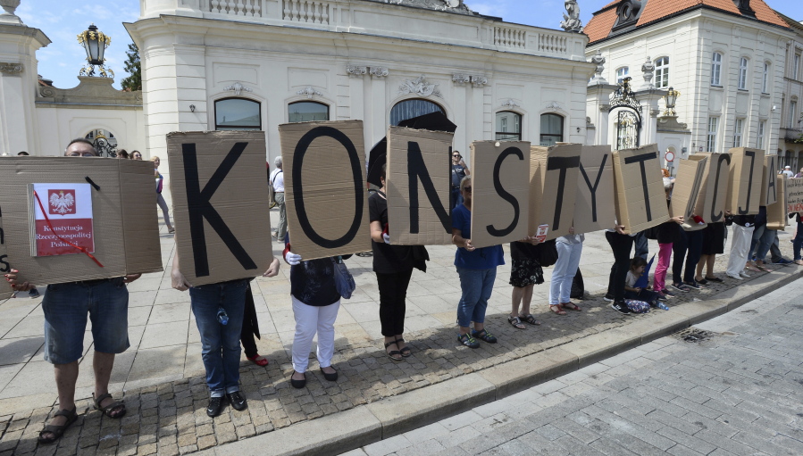 People hold boards with the word “Constitution” in front of the presidential palace Warsaw, Poland, Monday, July 24, 2017. Polish President Andrzej Duda announced that he will veto two contentious bills widely seen as assaults on the independence of the judicial system.