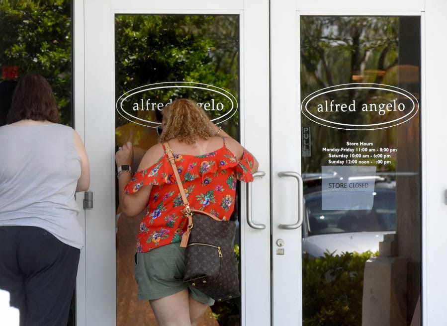 Women look into the closed Alfred Angelo Bridal store in Sunrise, Fla., in July after the business closed its doors and filed to liquidate its operations in bankruptcy court in West Palm Beach.
