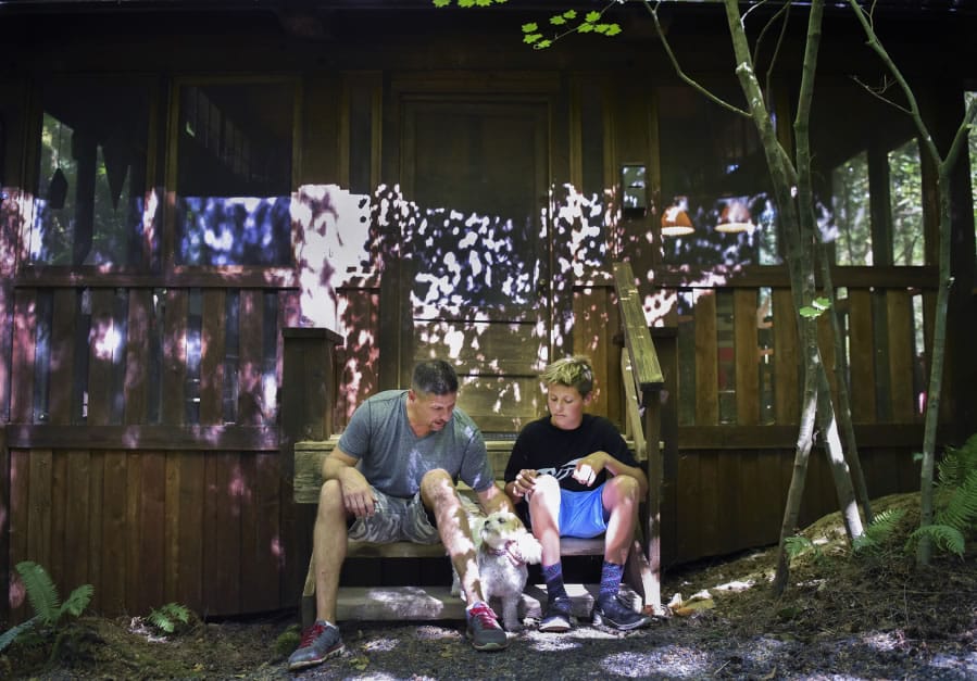 Neil Barnett, left, and his son Brayden Barnett, 13, pet their dog Lucy on the steps of their familyís screened deck at their campsite at Lake Merwin Campers Hideaway in Amboy.