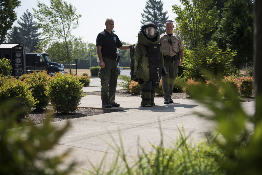 Above: Sheriff’s deputies Jeremy Koch, left, and Chris Luque lead 14-year-old Kenzie Brown, dressed in a full bomb suit, around a simulated crime scene to look for staged explosives. The Tuesday simulation was part of a full week of activities. Left: Deputies Chris Luque, left, and Jeremy Koch, right, help Jayden Pantier of Vancouver, 13, put on a bomb suit.