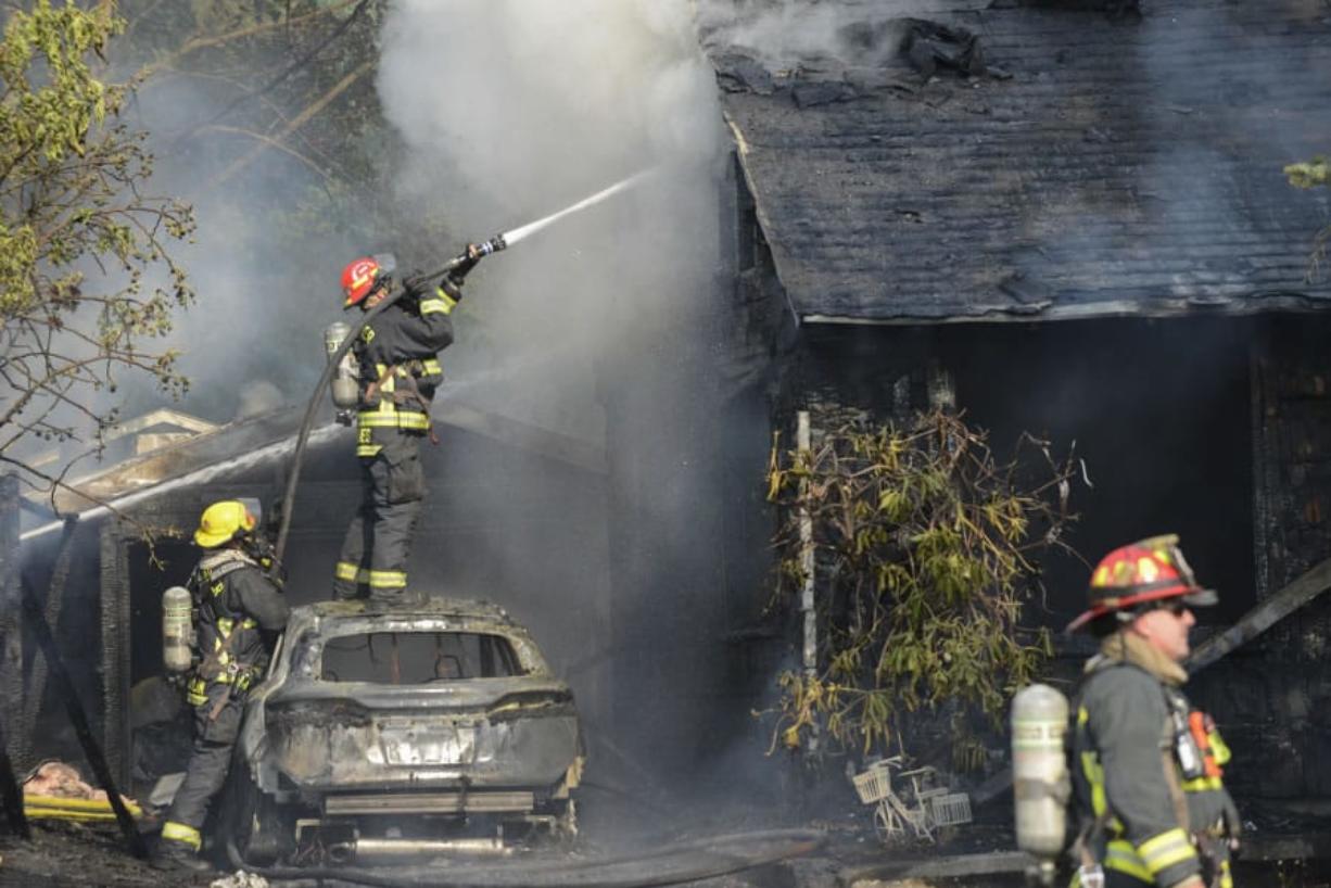 A Vancouver firefighter stands on top of a car in an attempt to put out a fire sparked by a malfunctioning battery charger. The fire destroyed one house and severely damaged a second on East Reserve Street in Vancouver.
