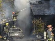 A Vancouver firefighter stands on top of a car in an attempt to put out a fire sparked by a malfunctioning battery charger. The fire destroyed one house and severely damaged a second on East Reserve Street in Vancouver.