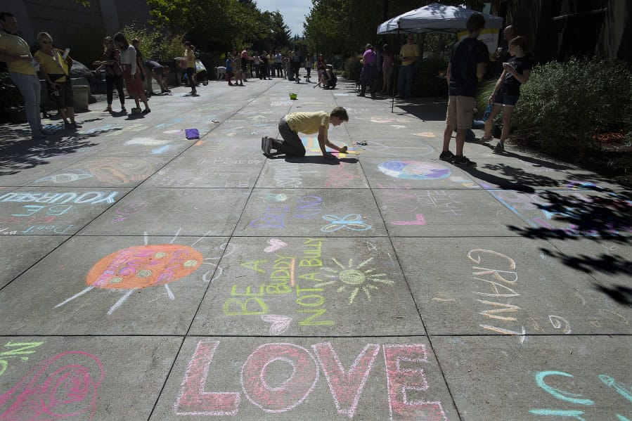 Words of love and kindness surround Joy Team member Denali Miller, 17, in yellow shirt, as he adds a little color outside Vancouver City Hall during the annual Chalk the Walks event on Tuesday.