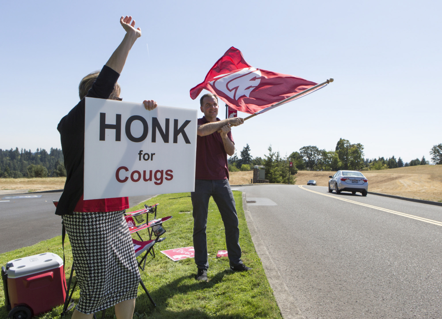 Andy Bao/The Columbian Academic Coordinator Mary Stender, left, and IT systems specialist Aaron Thorne welcome new and returning students to the first day of fall semester at Washington State University Vancouver on Monday afternoon, waving the Cougar flag to passing motorists.