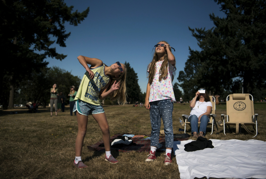 Kayden Williams, 9, left, and her sister Kendall, 11, both of Camas, follow the solar eclipse as it passes through the darkest point Monday morning at Fort Vancouver National Historic Site. “It looked like the Cheshire Cat, but without the eyes,” Kayden said.