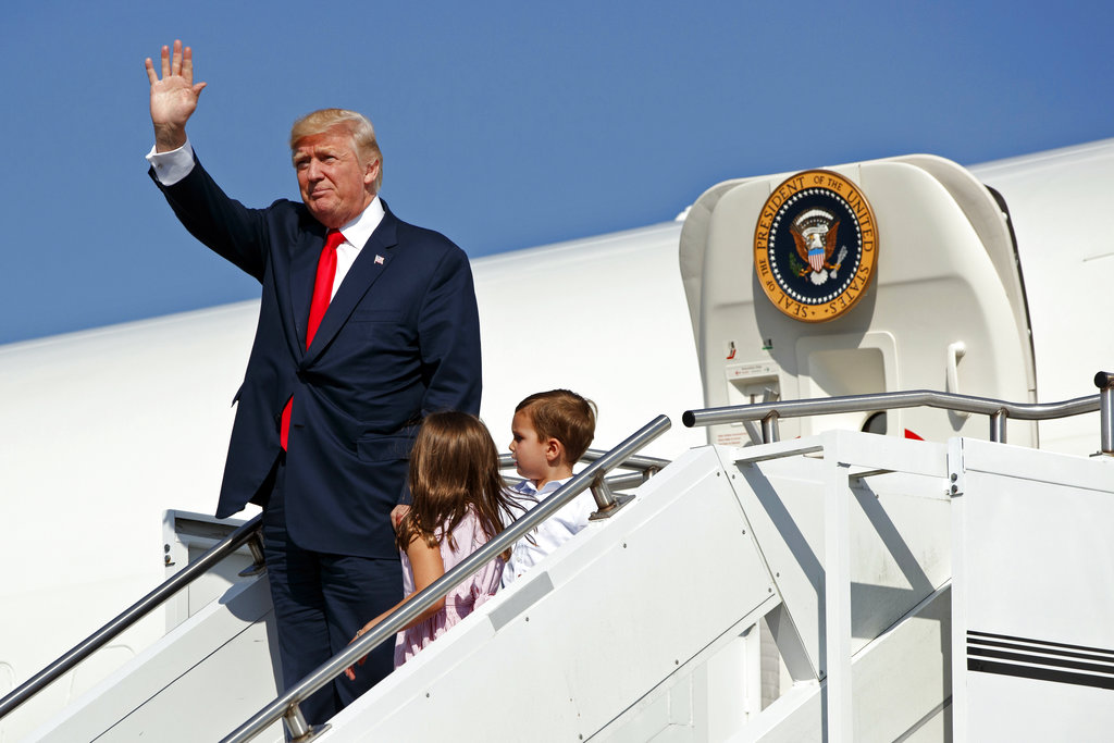 FILE- In this Aug. 4, 2017, file photo, President Donald Trump waves as he walks down the steps of Air Force One with his grandchildren, Arabella Kushner, center, and Joseph Kushner, right, after arriving at Morristown Municipal Airport to begin his summer vacation at his Bedminster golf club in Morristown, N.J. The president has decamped from Washington to his private golf club in central New Jersey. But he has repeatedly pushed back on the idea that this is a relaxing August getaway.