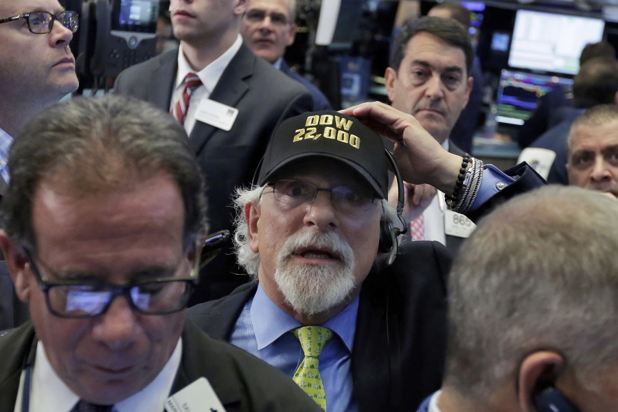 Trader Peter Tuchman, center, wears a “Dow 22,000” hat as he works on the floor of the New York Stock Exchange, Wednesday. A big gain from Apple Wednesday morning sent the Dow Jones industrial average above 22,000 for the first time. Most other industries were trading lower, with health care and household goods companies slipping.