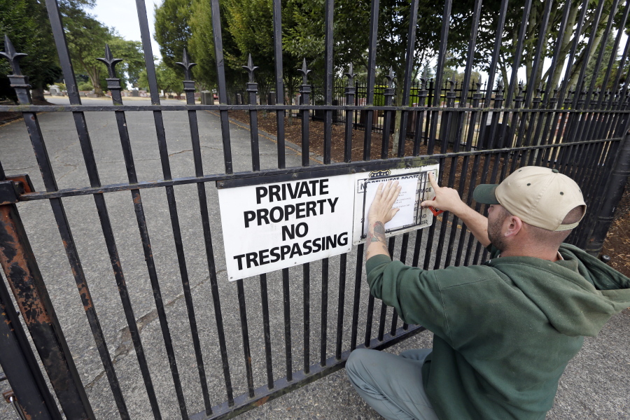 A worker, who declined to be identified, posts a notice of temporary closure on the locked gates of Lake View Cemetery, which was shut following angry messages they’ve received over a memorial for Confederate soldiers, Thursday, Aug. 17, 2017, in Seattle. The private cemetery was shut down a day earlier and is expected to remain closed through the weekend over a memorial that’s stood there nearly a century and now there’s a petition asking for it to come down. The memorial was built with help from the Daughters of the Confederacy 91 years ago.