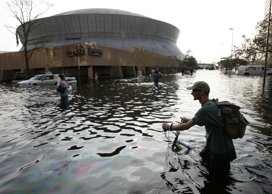 FILE - This Aug, 31, 2005, file photo shows a man pushing his bicycle through flood waters near the Superdome in New Orleans after Hurricane Katrina left much of the city under water. Some of those now taking shelter from Tropical Storm Harvey at Houston’s main convention center may be having flashbacks to a previous storm. Elected officials in Texas are promising to heed the lessons from Katrina, which resulted in hundreds of deaths and tens of billions of dollars in damage.