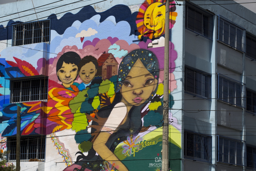 A woman fleeing with her children and her home on her back is depicted on a street mural being painted in Mexico City by asylum seekers and artist Eva Bracamontes.