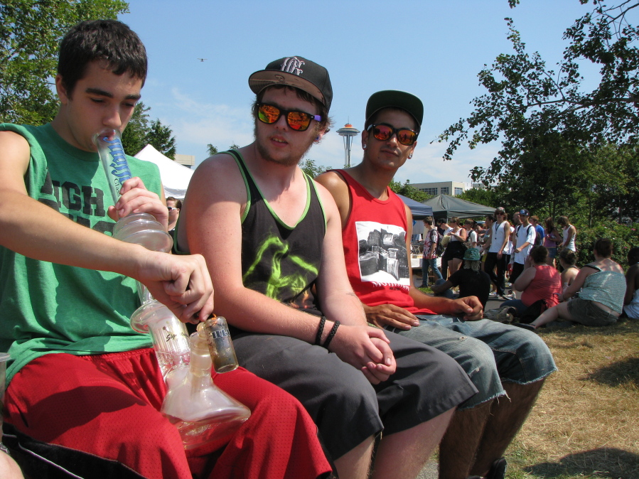 FILE--In this Aug. 17, 2012, file photo, Matt Galanti, 17, of Bothell, Wash., left, smokes marijuana from a glass bong at the opening day of the pro-marijuana rally Seattle Hempfest as friends Zach Casselman, 18, of Bothell, and Clay Graeber, 20, of Bothell, look on. Seattle on Tuesday, Aug. 8, 2017, agreed to drop a $1,000 fine issued to the nonprofit organization that runs HempFest--the annual summer marijuana celebration. The city accused the organization of operating a marijuana business without a license but later said it had no evidence the group violated the law.