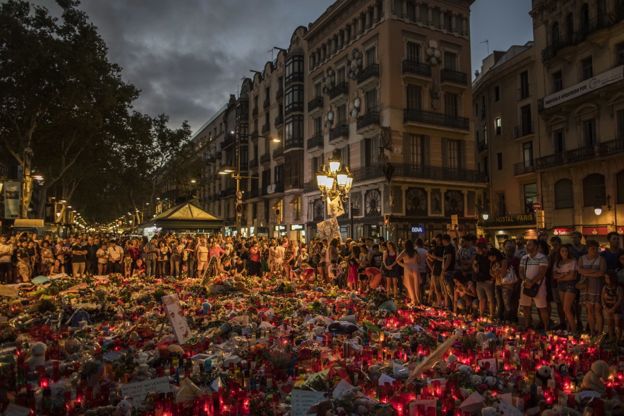 People stand next to candles and flowers placed on the ground, after a terror attack that left many killed and wounded in Barcelona, Spain, on Monday. The lone fugitive from the Spanish cell that killed 15 people in and near Barcelona was shot to death Monday after he flashed what turned out to be a fake suicide belt at two troopers who confronted him in a vineyard just outside the city he terrorized, authorities said.