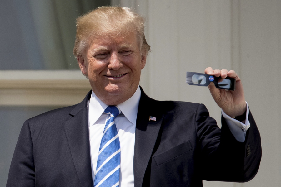 President Donald Trump holds up protective glasses as he arrives to view the solar eclipse at the White House in Washington, Monday, Aug. 21, 2017.