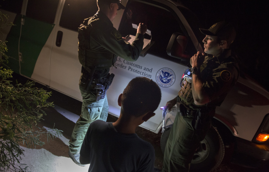Border Patrol agents Edgar Cano, right, and Richard Schweitzer, left, process unaccompanied minor Darwin, 11, center, for transportation after the boy illegally crossed the Rio Grande on a raft in Hidalgo, Texas, on March 24.