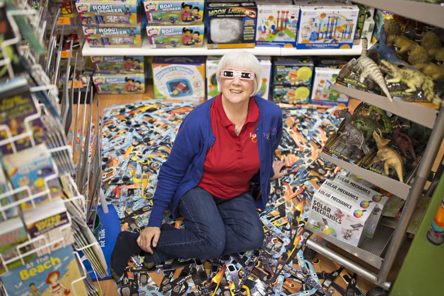 Mary Sisson, co-owner of Kazoodles toy store, sits among 400 sets of eclipse glasses Friday. The store in east Vancouver is among three local sites collecting eclipse glasses for Astronomers Without Borders, which will send them to schools in Asia and South America for eclipses in 2019.