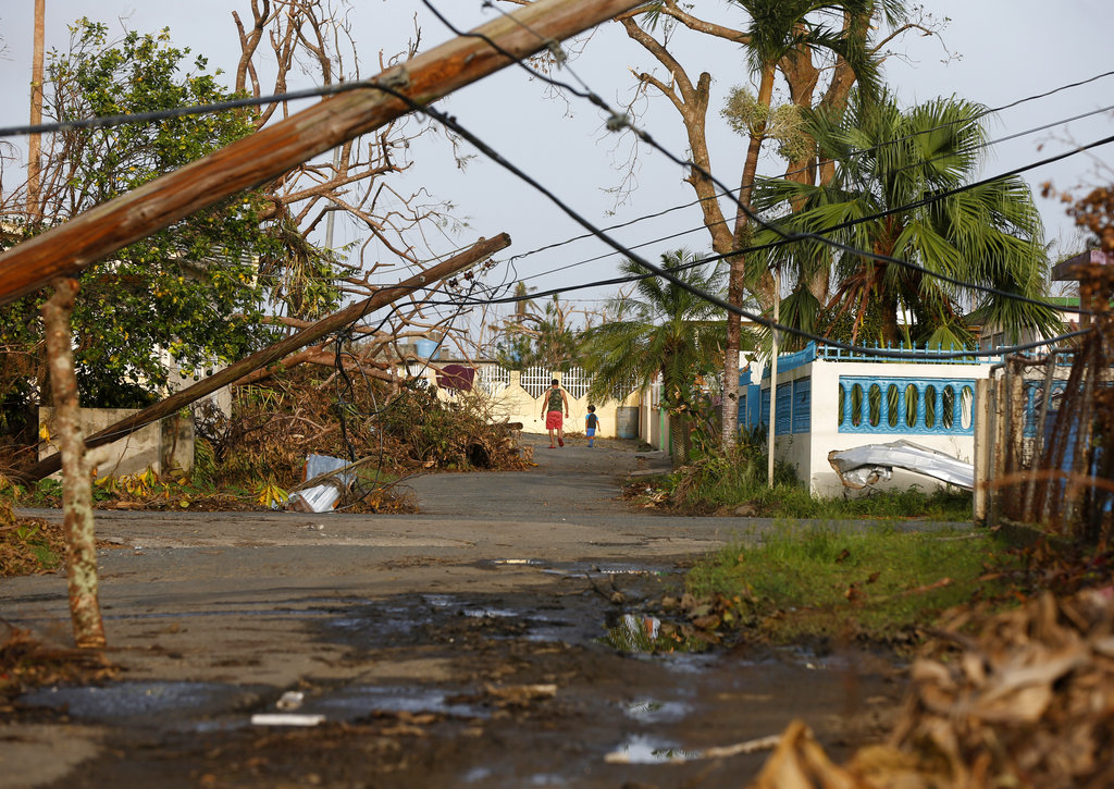 A man and child walk down street strewn with debris and downed power lines in the aftermath of Hurricane Maria, in Yabucoa, Puerto Rico, Tuesday, Sept. 26, 2017.
