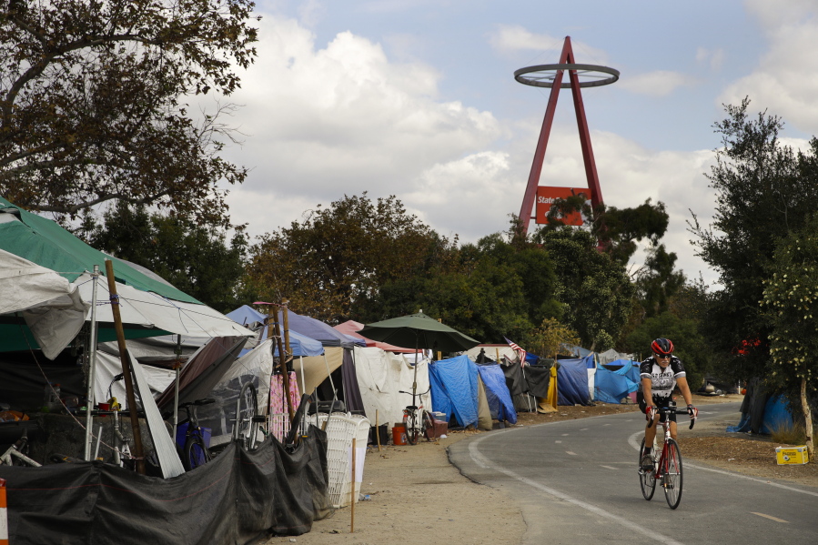 A cyclist passes the row of tents and tarps along the Santa Ana riverbed near Angel Stadium Thursday in Anaheim, Calif. Amid an uproar from residents, the city of Anaheim declared an emergency Wednesday in an attempt to cope with a ballooning homeless encampment along a popular riverbed trail and speed the addition of shelter beds. (AP Photo/Jae C.