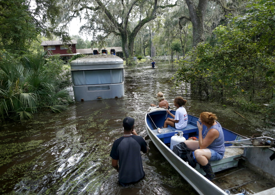 Family members ride in a small boat toward Tony Holt’s flooded trailer Thursday in Gainesville, Fla.